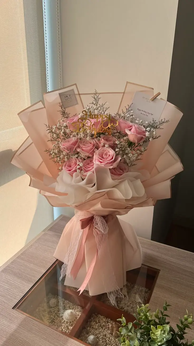 A bouquet of pink roses and baby's breath wrapped in elegant pink and white paper sits on a table, bathed in warm sunlight, evoking a romantic mood.