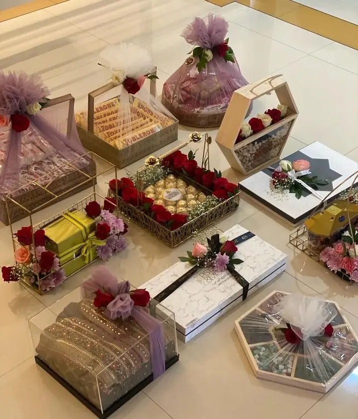 Elegant arrangement of gift boxes on a tiled floor, adorned with red roses and decorative wrapping. The setup conveys luxury and celebration.